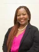 A woman with long hair and pink shirt in front of white wall.