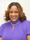 A woman in purple shirt and necklace smiling.