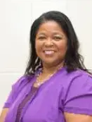 A woman in purple shirt and necklace smiling.