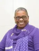 A woman in purple sweater and scarf smiling.