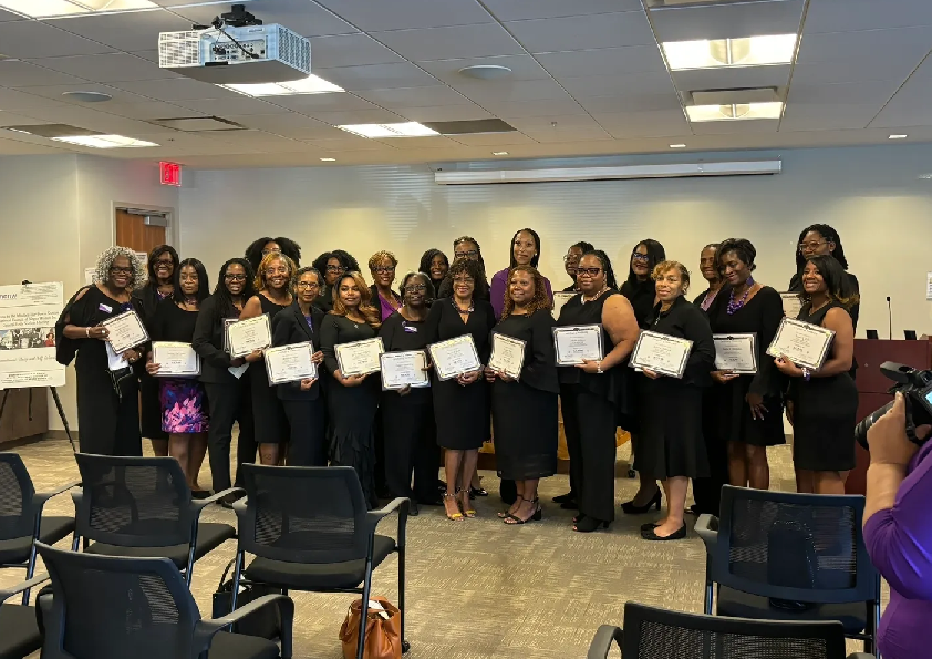 A group of women standing in front of chairs.