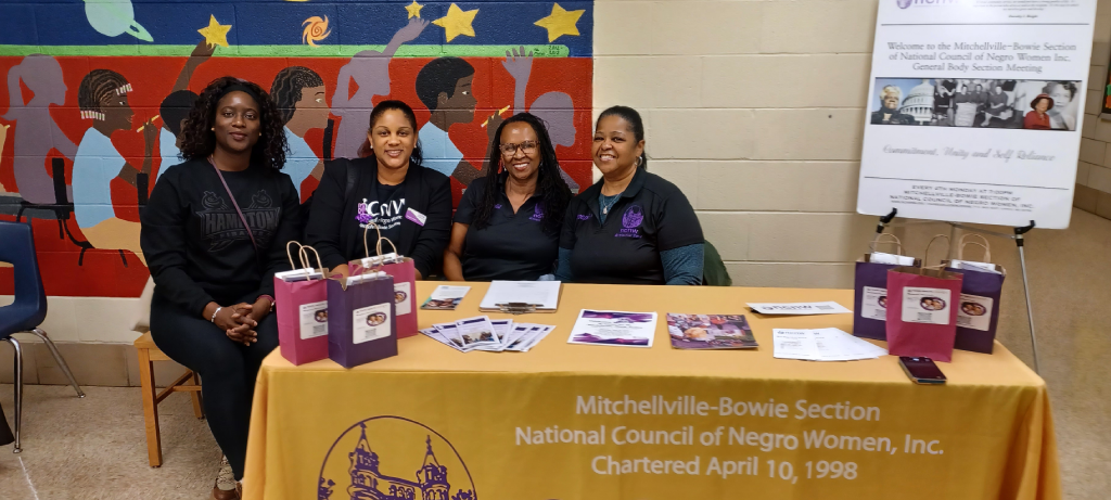 Three women sitting at a table with purple bags.