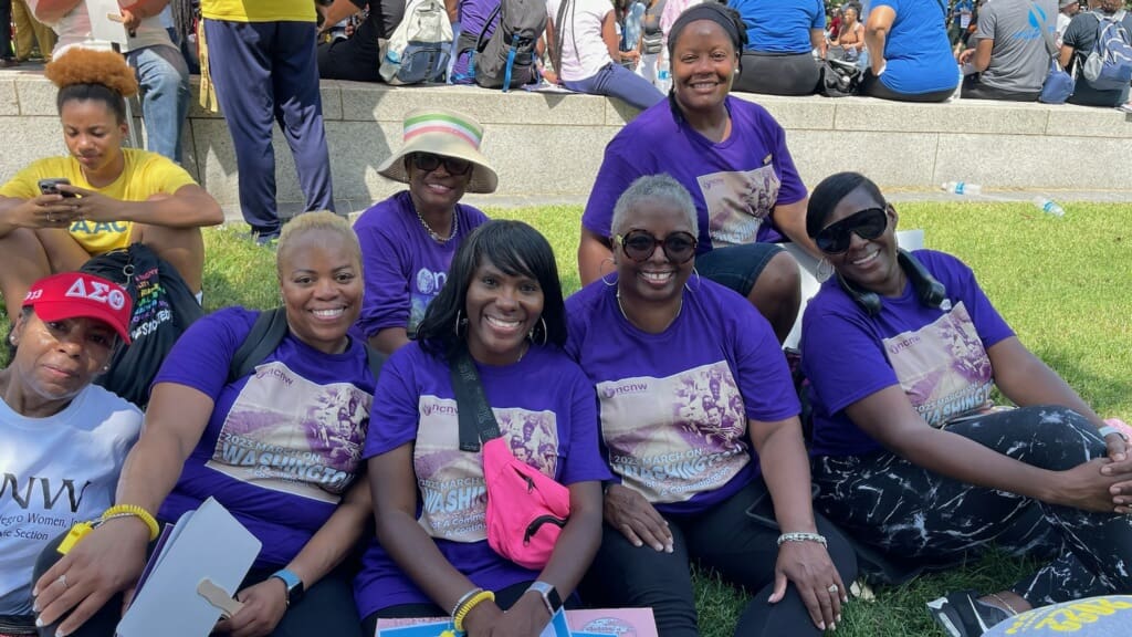 A group of people sitting on the grass wearing purple shirts.